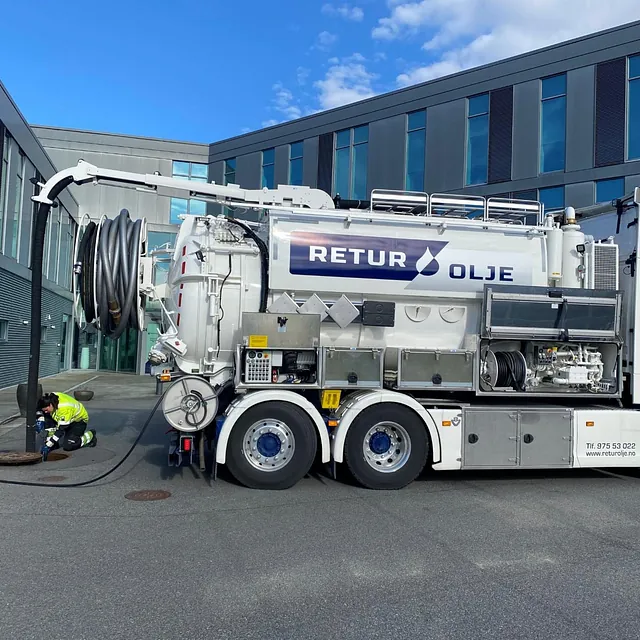 Hvit tankbil med slanger som går ned i bakken