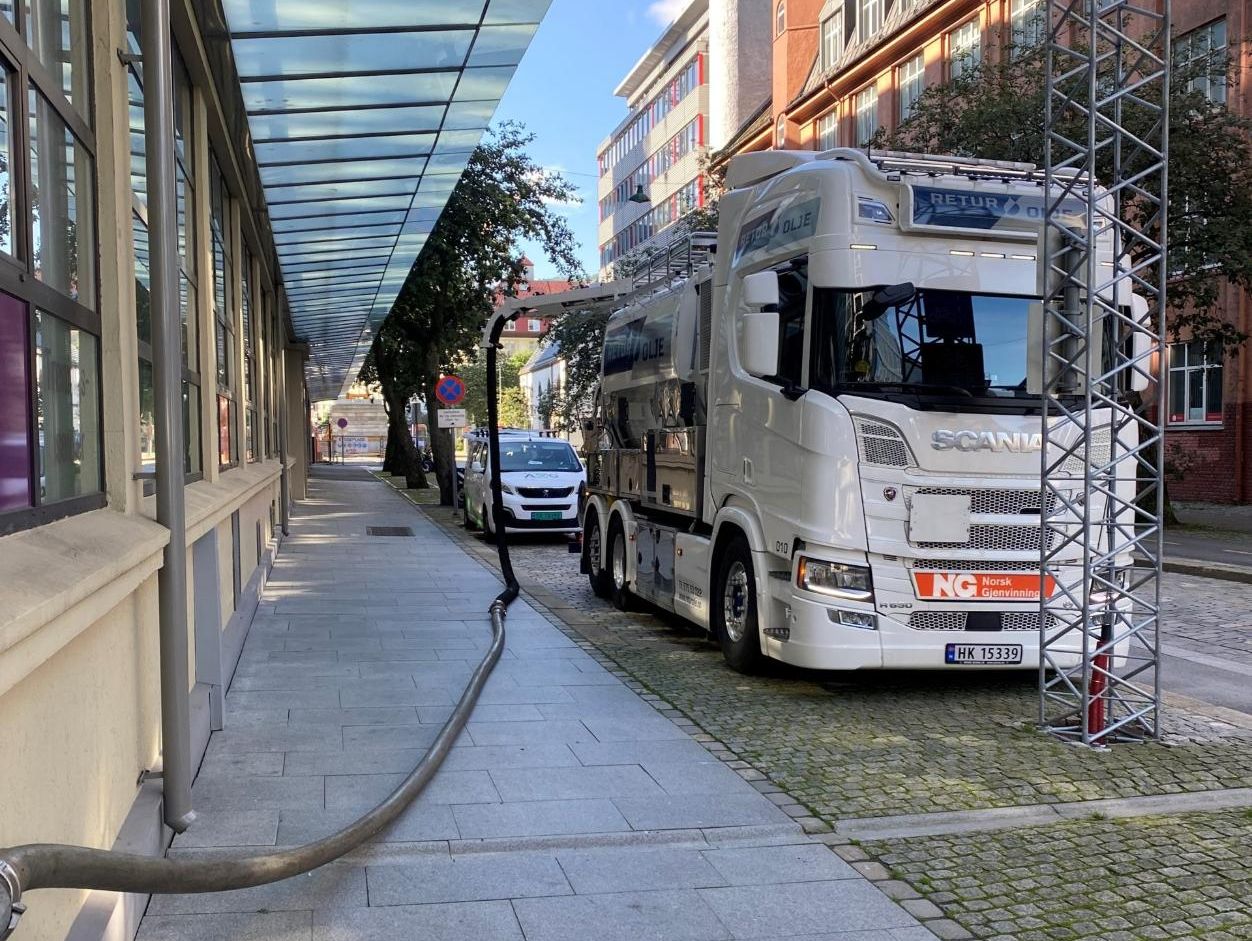 Hvit tankbil med slanger som går inn i bygg