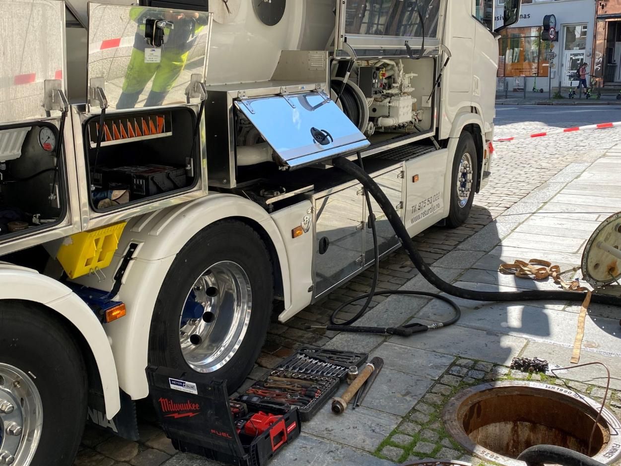 Hvit tankbil med slanger som går ned i bakken